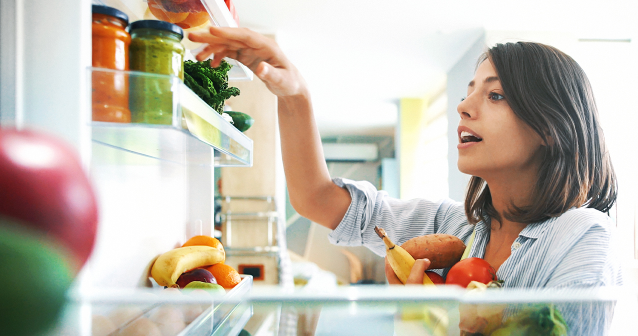 Frau am Kühlschrank ordnet gesunde Lebensmittel ein