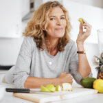 Lächelnde Frau in der Küche sitzt vor Obst & Gemüse