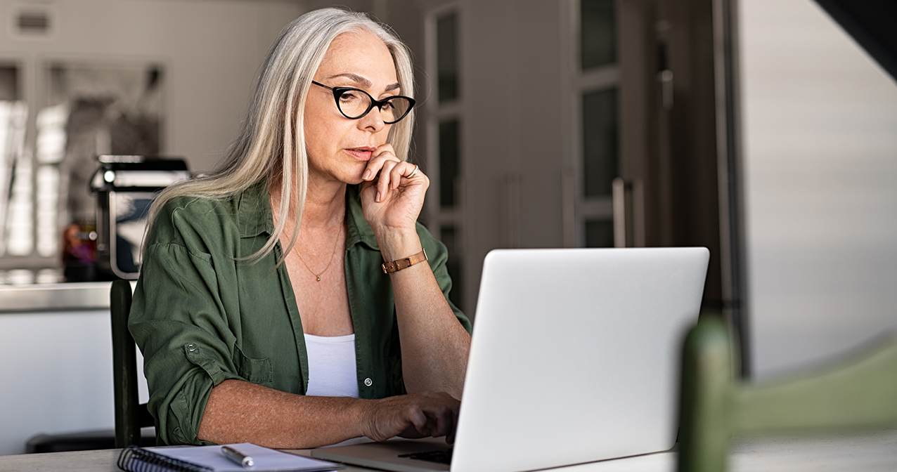 Grübelnde Frau mit Brille sitzt vor einem Laptop