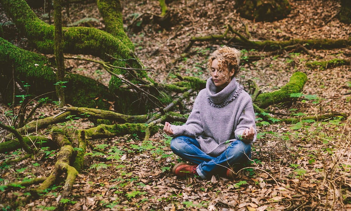 Frau meditiert auf dem Waldboden