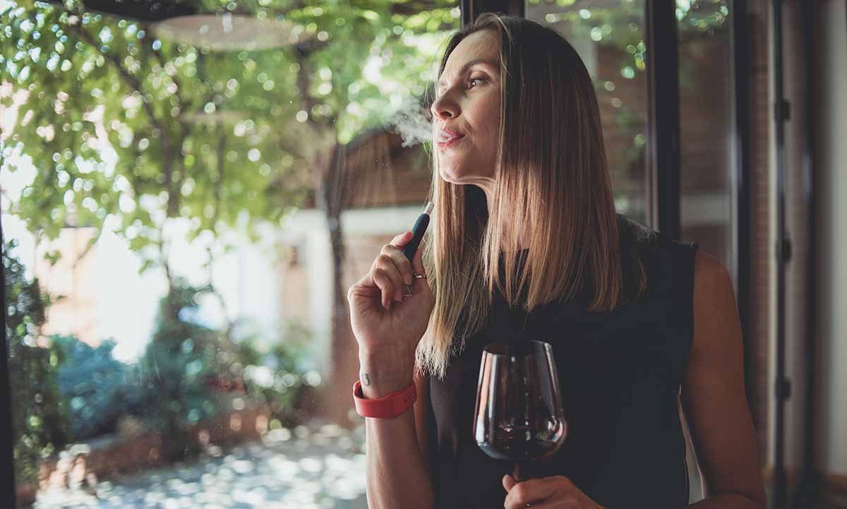 Frau raucht und hält ein Glas Wein in der Hand