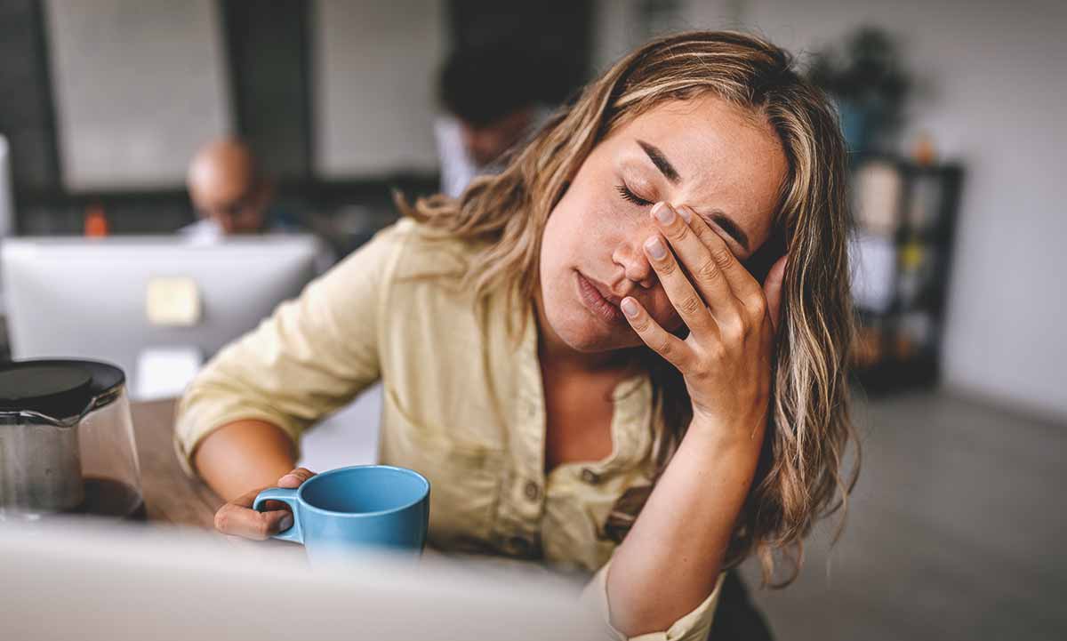 Frau mit Tasse in der Hand reibt sich die Augen