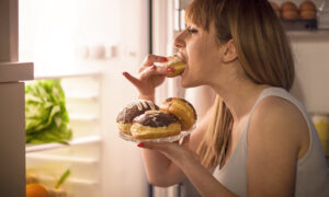 Frau steht am Kühlschrank und isst Donut