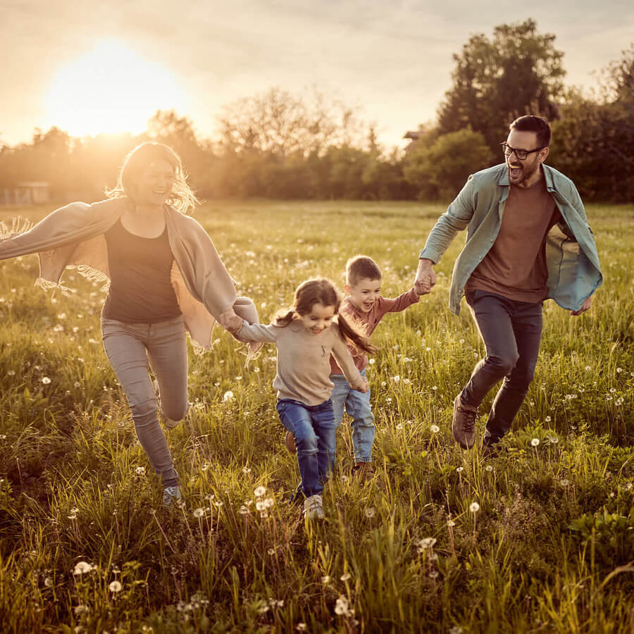 Eltern mit zwei Kindern auf Wiese bei Sonnenuntergang