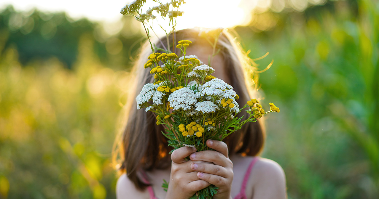 Kind hält Pflanzen und Kräuter in der Hand: Ganzheitliche Kindergesundheit