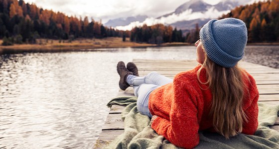 Frau liegt auf Steg und überschaut herbstlichen See