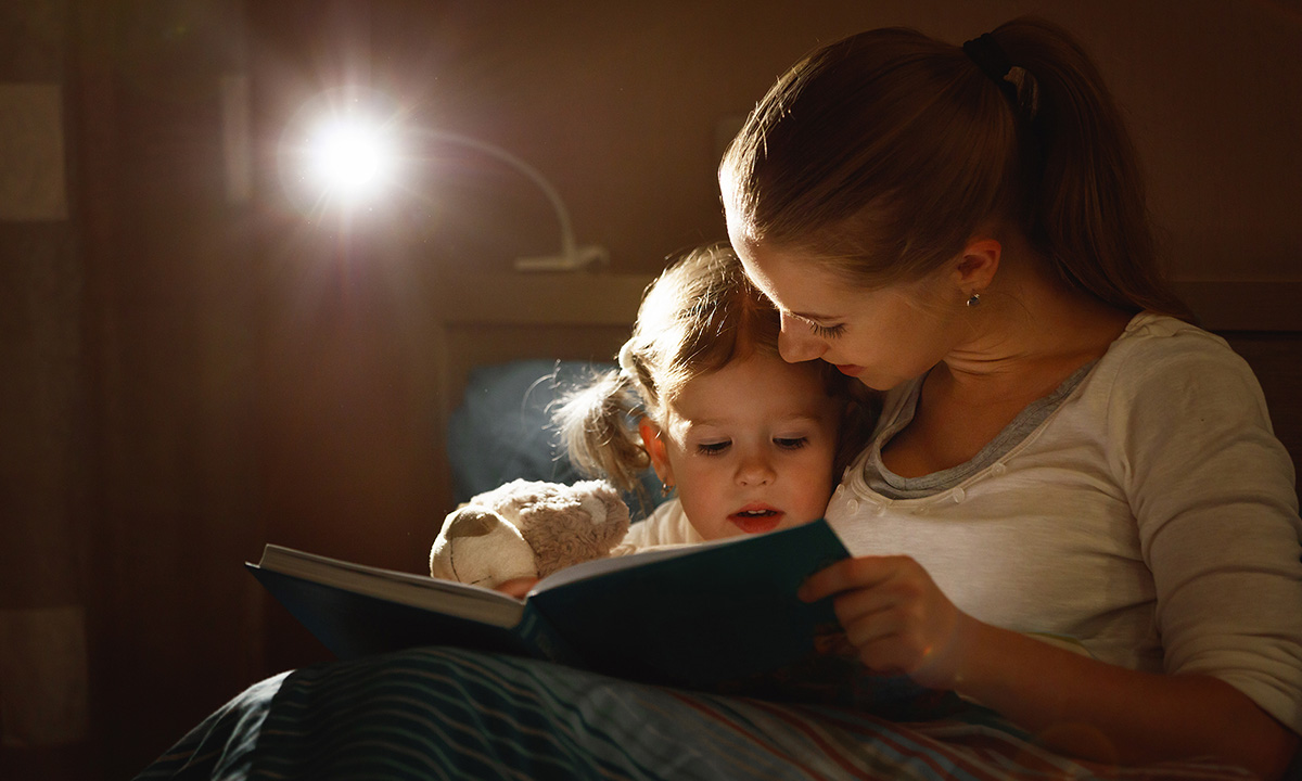 Kleinkind und Mama sitzen im Bett und lesen.