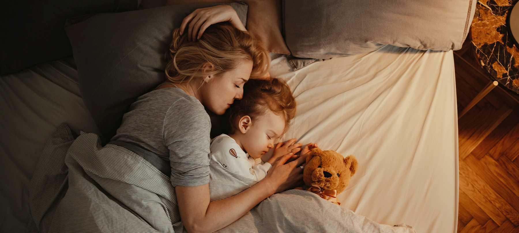 Mama und Kind liegen schlafend mit Teddybär im Bett – Blog Einschlafrituale