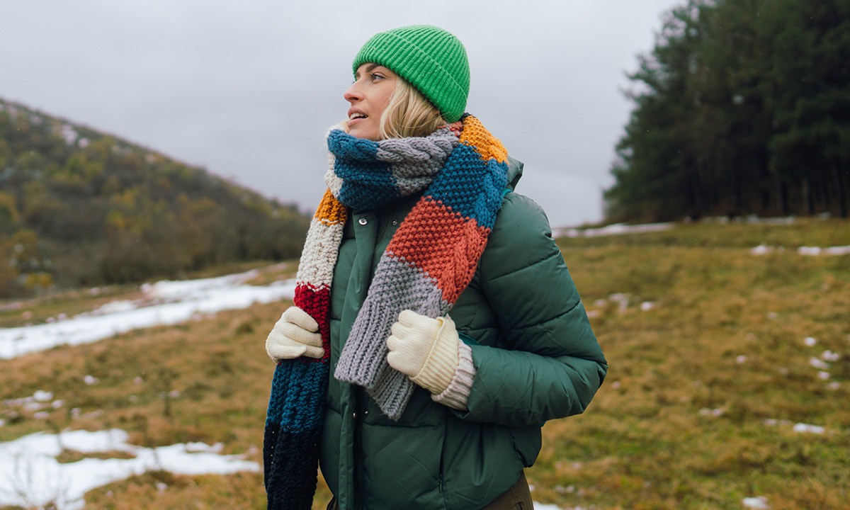 Frau mit Jacke, Schal & Mütze draußen in den Bergen