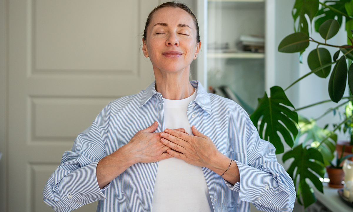 Frau, die ihre Hände auf der Brust hält und tief einatmen.