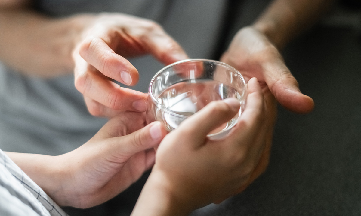 Erwachsener reicht Kind Glas Wasser